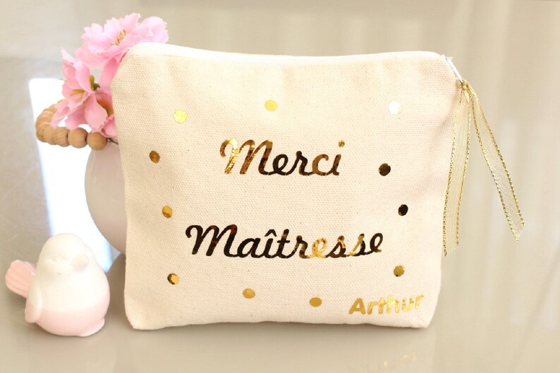 May include: A white canvas zippered pouch with gold glitter dots and the text "Merci Maitresse Arthur" in gold lettering.
