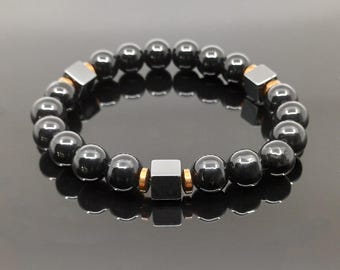 May include: Black hematite beaded bracelet with gold accents. The bracelet features square hematite beads interspersed with round black beads.
