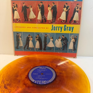 May include: A vintage vinyl record and album cover. The album cover features the text "GLENN MILLER GREATS!" and images of couples dancing. The record is a translucent orange colour with a blue label that reads "STEREO".