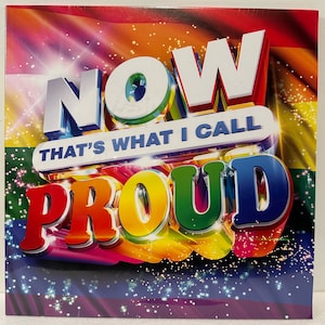 May include: A square music album cover featuring the text NOW THAT'S WHAT I CALL PROUD in bold, three-dimensional white and multicoloured lettering. The background displays a vibrant rainbow flag pattern with sparkling light effects throughout.