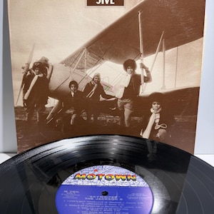May include: A vintage vinyl record album titled Skywriter by The Jackson 5, featuring a sepia-toned cover image of the group standing in front of a biplane. The black vinyl disc in the foreground displays a blue Motown label with track listings.