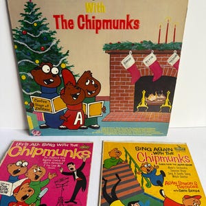 May include: Three vintage vinyl record covers featuring The Chipmunks. The top cover shows a Christmas tree and fireplace with the text The Twelve Days Of Christmas With The Chipmunks. The bottom covers are titled Let's All Sing With The Chipmunks and Sing Again With The Chipmunks, both featuring illustrations of the characters and David Seville.