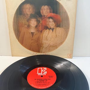 Puede incluir: Álbum de vinilo vintage de The Incredible String Band, con una foto de grupo en un marco circular. La portada del álbum es beige con texto. Un disco de vinilo negro con una etiqueta roja de Elektra está en primer plano.