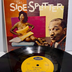 Może przedstawiać: Vintage winylowy album zatytułowany "The Side-Splitter" autorstwa Rodda Foxxa. Okładka albumu przedstawia kobietę trzymającą poduszkę i mężczyznę pokazującego znak pokoju. Etykieta płyty jest żółta z czarnym tekstem.