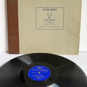 Könnte beinhalten: Ein Vintage-Schallplatten-Set mit einem hellbeigen Albumcover, einem braunen Buchrücken und schwarzem Text mit der Aufschrift SCHUBERT Fantasie, Edward Kilenyi und Columbia Masterworks Set M-426. Eine schwarze Schallplatte mit blauem Label liegt davor.