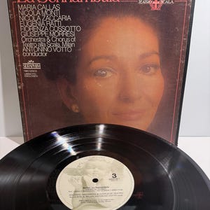 May include: A black vinyl record and its square cardboard sleeve featuring a portrait of Maria Callas. The cover text reads Bellini La Sonnambula, Teatro alla Scala, and lists the cast and conductor. The record label shows a cherub illustration.