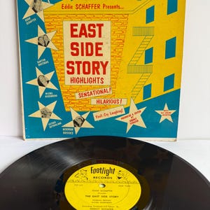 May include: A vintage vinyl record and its square cardboard sleeve. The yellow and blue cover features the text East Side Story Highlights, All Star Fun Packed Revue, and Footlight Records, with star-shaped portraits of performers.