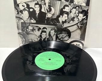 May include: A black vinyl record with a green label. The label has the text "The Great Music Company" and "The Elvis Tapes" on it. The record is a part of a larger image that shows a collage of black and white photos of Elvis Presley.