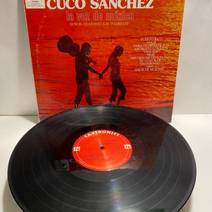 May include: A vinyl record album cover with a red, orange, and white background. The cover features a photo of two people standing in the water. The album title is "Puerto Rico Cuco Sanchez la voz de mexico" with the text "Con el Cuarteto Los "Padrinos"" below. The album is by Caytronics and has the catalog number CYS 1435.