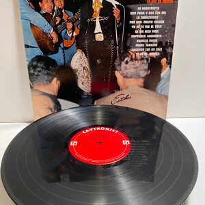 May include: Vinyl record album cover featuring a photo of a man in a charro suit with a mariachi band. The album title is "Cuco Sanchez" and the text "La Voz de Mexico" is below the title. The album cover is black and white.