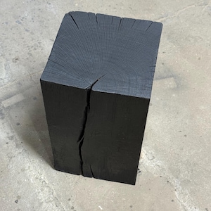 Op de afbeelding: Een vierkant, zwart houten blok met zichtbare nerf en een scheur aan één kant. Het blok is waarschijnlijk een kleine kruk of bijzettafel, met een minimalistisch ontwerp. Afmetingen: ongeveer 30 cm x 30 cm x 45 cm.