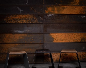 Könnte beinhalten: Drei Metallhocker mit Holzplatten. Die Hocker stehen vor einer rostigen Metallwand. Die Hocker haben unterschiedliche Höhen und ein modernes industrielles Design.