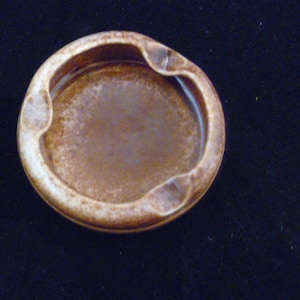 May include: A brown ceramic ashtray with a white rim. The ashtray has a slightly raised edge around the center.