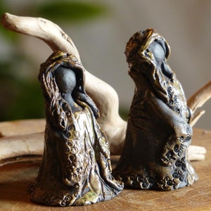 Könnte beinhalten: Zwei Keramikfiguren von verhüllten Figuren mit detaillierten goldenen und braunen Mustern. Die Figuren stehen auf einem Stück Treibholz.