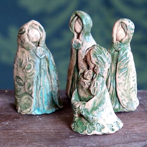 Könnte beinhalten: Vier Keramikfiguren von Frauen, die grüne und blaue Umhänge mit komplizierten Designs tragen. Die Figuren stehen im Kreis und schauen sich an.