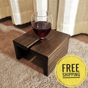 May include: A dark brown wooden stand with a unique design that allows a glass to rest securely on top. The stand is perfect for holding a glass of wine or other beverages.