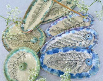 May include: A collection of oval and round ceramic incense holders featuring embossed fern leaf patterns. Each piece has a glazed finish in shades of cream, blue, and green, with a small raised bead for holding an incense stick.