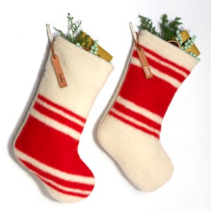Peut inclure: Deux chaussettes de Noël rayées blanches et rouges avec des étiquettes en cuir. Les chaussettes sont suspendues et remplies de petits cadeaux et de verdure. Les étiquettes indiquent "Sophia" et "James".