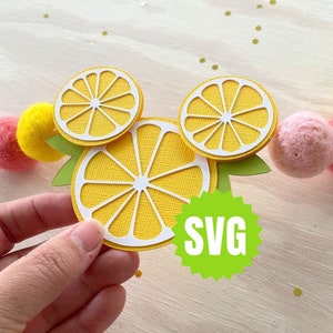 May include: A set of three yellow lemon-shaped paper cutouts with white centers and green leaves. The cutouts are arranged in a Mickey Mouse shape. The text "SVG" is on a green starburst.