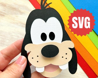 May include: A papercraft cutout of Goofy's face. The cutout is made of black, white, brown, and pink paper. The cutout is held in a hand against a rainbow background. The word "SVG" is in a red starburst.