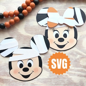 Puede incluir: Recortes de papel con temática de Halloween de Mickey y Minnie Mouse. Mickey tiene una venda en la cabeza y Minnie lleva un lazo. Los recortes son negros, blancos y naranjas, con un tono de piel melocotón claro. También hay un logotipo SVG naranja.
