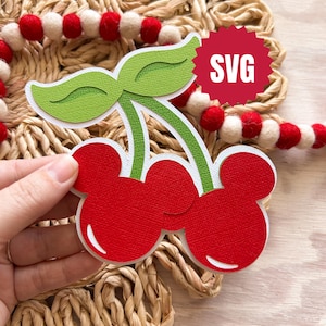 Puede incluir: Archivo de corte SVG de cereza roja y verde. La cereza es de estilo de dibujos animados con un tallo y dos hojas. La cereza está sobre un fondo tejido.