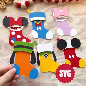 Può includere: Una collezione di calze di Natale di carta colorate in vari disegni. Le calze presentano personaggi con fiocchi, orecchie e altri dettagli. Le calze sono rosse, blu, arancioni, gialle e rosa. Un logo SVG rosso si trova nell'angolo in basso a destra.