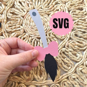 May include: A pink bow with a black and white broom stick attached to a gray handle. The handle has a gray circle on the top. The bow and broom are on a woven straw background. The word "SVG" is written in black on a pink starburst.