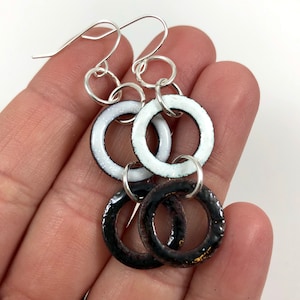 Op de afbeelding: Een paar oorhangers met drie zwarte en witte keramische ringen aan elke oorhanger. De ringen zijn verbonden met zilveren springringen en hangen aan zilveren oorhaken.