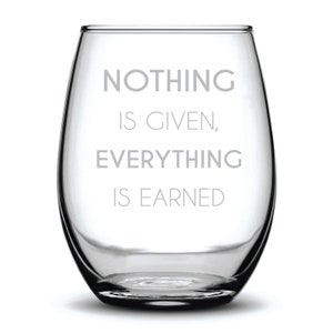 May include: A clear stemless wine glass with the words "NOTHING IS GIVEN, EVERYTHING IS EARNED" etched in a gray font. The glass has a rounded shape and is designed for wine.