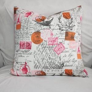 Op de afbeelding: Een witte kussenhoes met een roze en oranje vintage postzegelontwerp. De kussenhoes heeft verschillende postzegels met handschrift en de woorden "RTE POSTA".