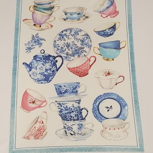May include: A decorative tea towel featuring watercolor illustrations of teacups, saucers, and a teapot in various colors, including blue, pink, and white. The design includes floral patterns and a blue border.