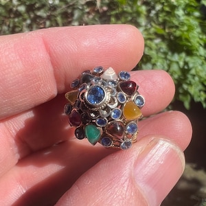 Puede incluir: Un anillo de oro con un grupo de piedras preciosas de colores, incluyendo azul, verde, rojo, amarillo y marrón. El anillo está engastado con una variedad de piedras, incluyendo zafiros, esmeraldas, rubíes y citrinos.