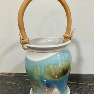 May include: A white ceramic planter with a blue, green, and brown glaze. The planter has a bamboo handle.