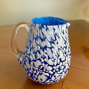 May include: A blue and white glass pitcher with a textured, marbled design. The pitcher has a clear handle and a blue rim.