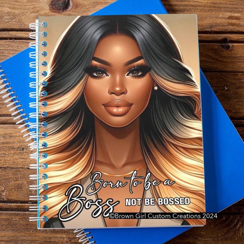 May include: A spiral bound notebook featuring a colourful illustration of a woman with long, wavy hair. The text "Born to be a Boss Not Be Bossed" is printed on the cover. The copyright information "Brown Girl Custom Creations 2024" is also printed on the cover.