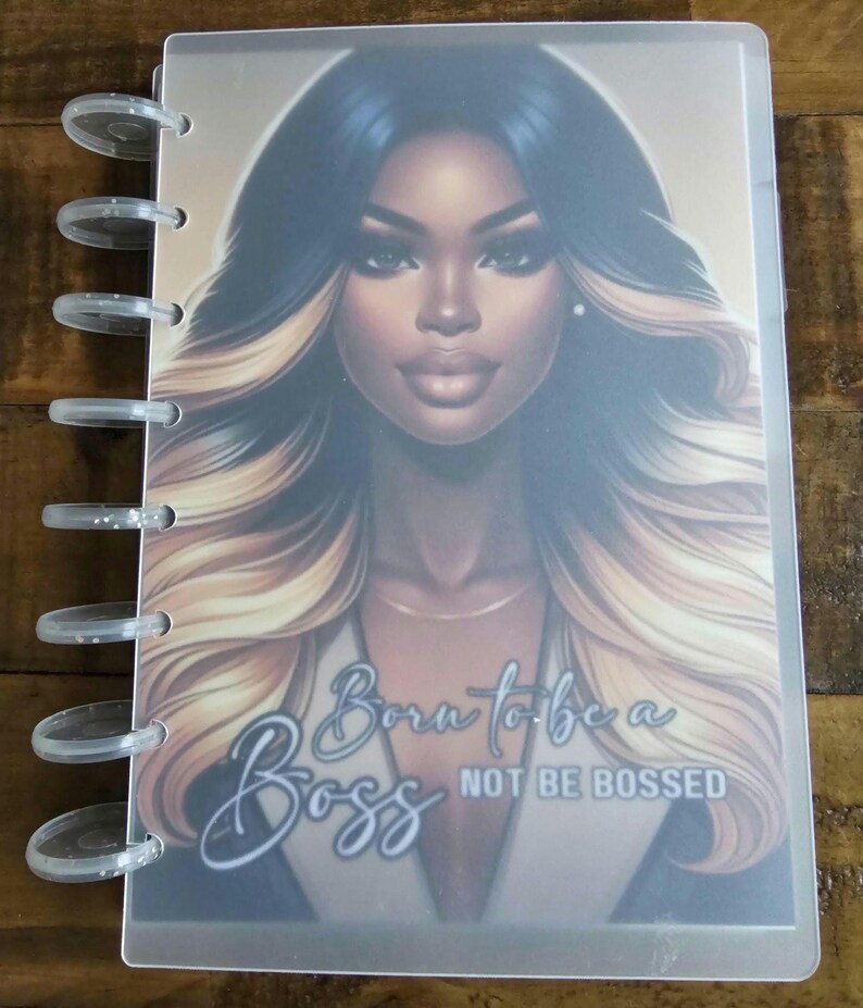 May include: A clear plastic cover for a planner featuring a colourful illustration of a woman with long blonde and brown hair. The text "Born to be a Boss Not Be Bossed" is printed on the cover.