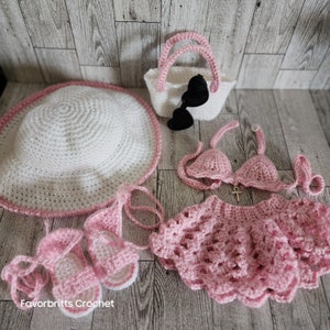 May include: A pink crocheted doll outfit with a white crocheted sun hat, a pink crocheted purse, and a pair of pink crocheted sandals. The outfit includes a bikini top and a skirt.