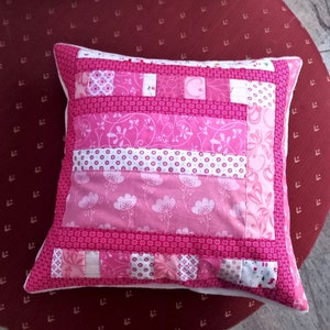 Puede incluir: Almohada de patchwork rosa y blanco con un patrón floral. La almohada está hecha de diferentes telas y tiene un borde blanco.