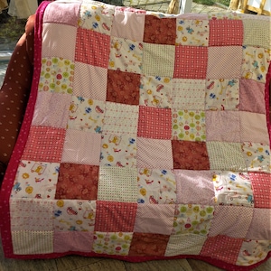 Peut inclure: Une courtepointe en patchwork rose et blanche avec une variété de motifs colorés, y compris des voitures, des animaux et des motifs géométriques.