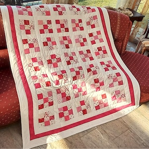 Könnte beinhalten: Eine Patchwork-Decke mit einem Raster aus Quadraten in verschiedenen Rosa-, Rot- und Weißtönen. Das Design besteht aus abwechselnden Blöcken mit Blumen- und geometrischen Mustern, umrahmt von einem weißen Rand und einer leuchtend rosa Borte.