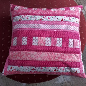 Peut inclure: Un oreiller rayé rose et blanc avec un motif patchwork. L'oreiller est fait de différents tissus avec des motifs floraux et géométriques.