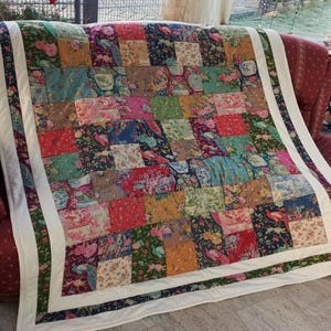 May include: A patchwork quilt with a white border and a variety of floral patterns in shades of blue, green, red, and brown.