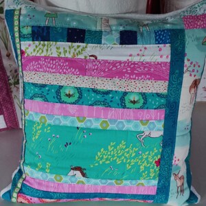 Könnte beinhalten: Ein türkisfarbenes und rosafarbenes Patchwork-Kissen mit einem floralen und tierischen Muster. Das Kissen besteht aus verschiedenen Stoffresten, die in einem horizontalen Muster zusammengenäht sind.