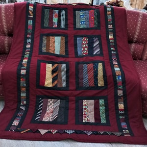 Könnte beinhalten: Eine burgunderfarbene Steppdecke mit schwarzem Rand und einem Patchwork-Muster aus verschiedenen Krawatten. Die Steppdecke besteht aus neun Quadraten, jedes mit einem anderen Muster aus Krawatten.