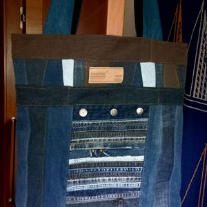 Könnte beinhalten: Eine blaue Jeans-Tragetasche mit braunem Stoff oben und einem Patch mit der Aufschrift "Sunbird". Die Tasche ist aus recyceltem Denim gefertigt und hat ein Patchwork-Design.