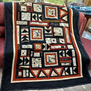 Könnte beinhalten: Eine schwarze und braune Quiltdecke mit musikalischem Thema. Die Decke besteht aus verschiedenen Quadraten und Dreiecken, die jeweils ein anderes musikalisches Design aufweisen. Die Decke ist mit einem schwarzen Stoff eingefasst und hat einen weißen Besatz.