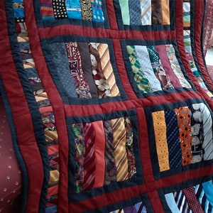 Può includere: Un quilt realizzato con cravatte riutilizzate. Il quilt è composto da quadrati di diversi colori e motivi. Il quilt è un patchwork di diverse cravatte, con ogni quadrato di un colore e un motivo diverso. Il quilt è un modo unico e creativo per riutilizzare vecchie cravatte.