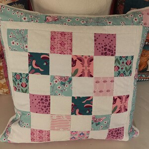 Può includere: Cuscino quadrato patchwork con sfondo bianco e quadrati con vari motivi floreali e di uccelli in verde acqua, rosa e viola. Il cuscino ha un bordo bianco e finiture floreali verde acqua.