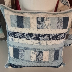 Puede incluir: Una almohada de patchwork azul y blanco con un patrón floral. La almohada está hecha de diferentes telas y tiene un borde blanco.